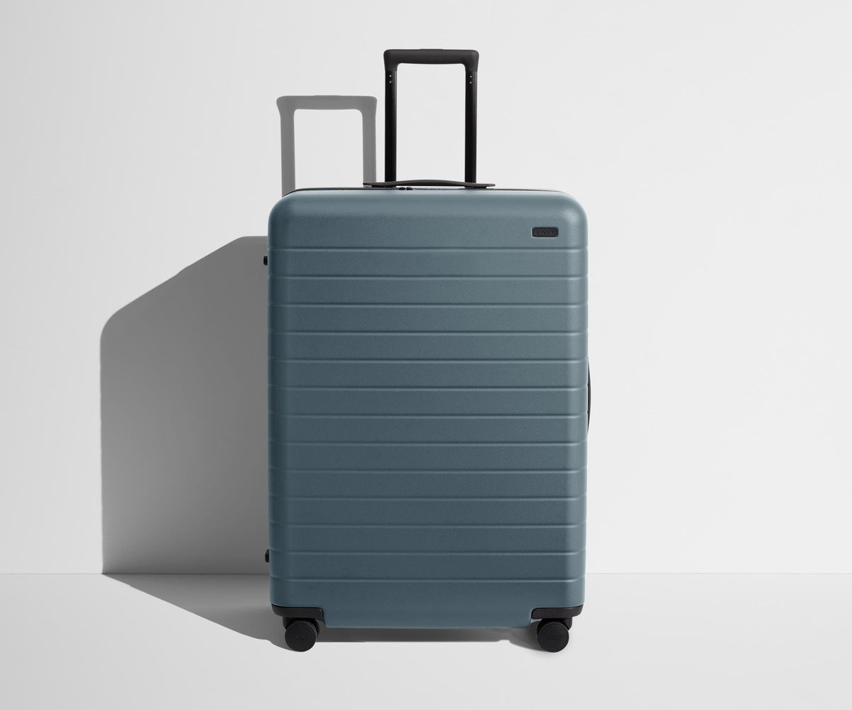 Blue suitcase with a black handle on a light gray background